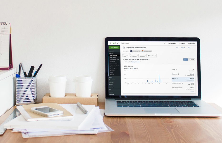 Laptop showing Clover sales dashboard on a desk with coffee cups and office supplies.