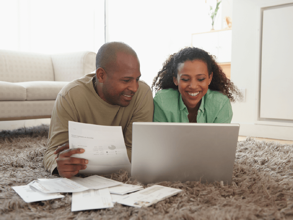 Couple laying on living room floor working on budget on laptop