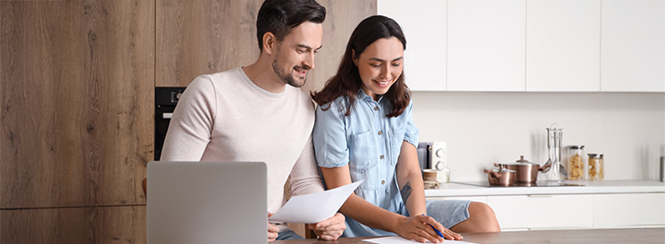 Couple reviewing 2024 goal progress in kitchen with laptop and papers