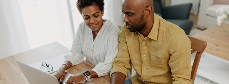 Couple sitting at kitchen table reviewing budget on laptop