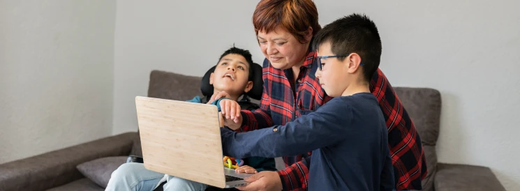 Mother and two sons sitting on couch looking at laptop