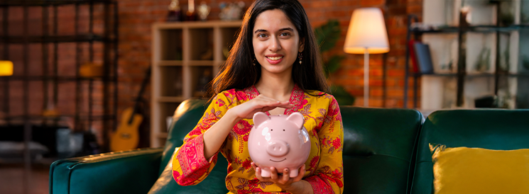 Woman sitting on couch holding pink piggy bank