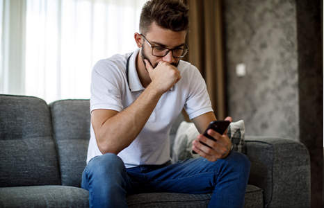 Man in white polo shirt looking at phone perplexed