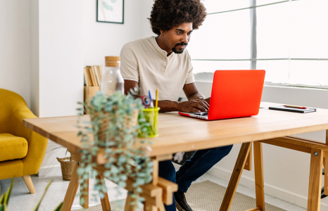 Man sitting at wooden desk using orange laptop to initiate balance transfer